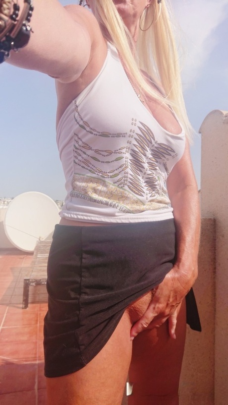 Naughty MILF Natalie K plays with her trimmed pussy while standing